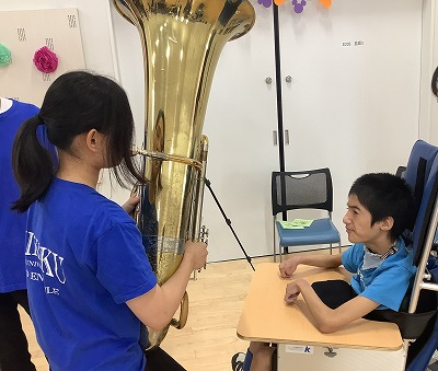 チューバ担当の学生が目の前で音を鳴らすのを高等部生徒が見ている写真
