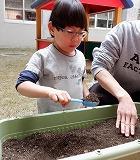 砂遊び用のスコップをもってプランターの土をすくっている写真