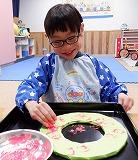 幼児が絵の具がついたピーマンを画用紙にスタンプしている写真