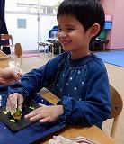 幼児が絵の具がついたピーマンをつまみ、折り紙にスタンプしている写真