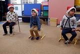 幼児がサンタ帽をかぶって椅子に座り、会の始まりを待っている写真
