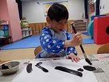 幼児が左手で半紙を押さえながら筆を動かしているところ