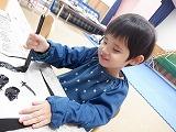 幼児が左手で半紙を押さえながら縦に筆を動かしているところ