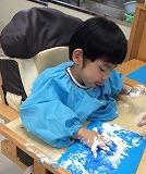 児童が画用紙の上でクリーム粘土を塗り広げている写真。
