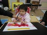 赤い絵の具のついた筆を持って書いている幼児の写真