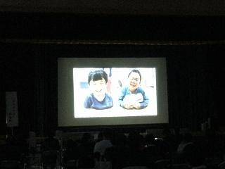 スクリーンに幼稚部の2名が並んで笑っている映像が映っている写真。