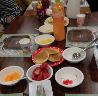 テーブルの上にホットケーキ、ジュース、トッピングの果物等が並べられています